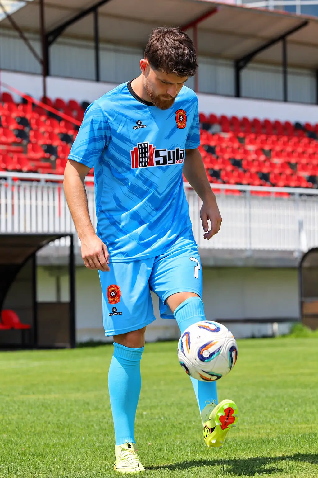 Futbollist me uniformë të kaltër duke mbajtur topin në ajër